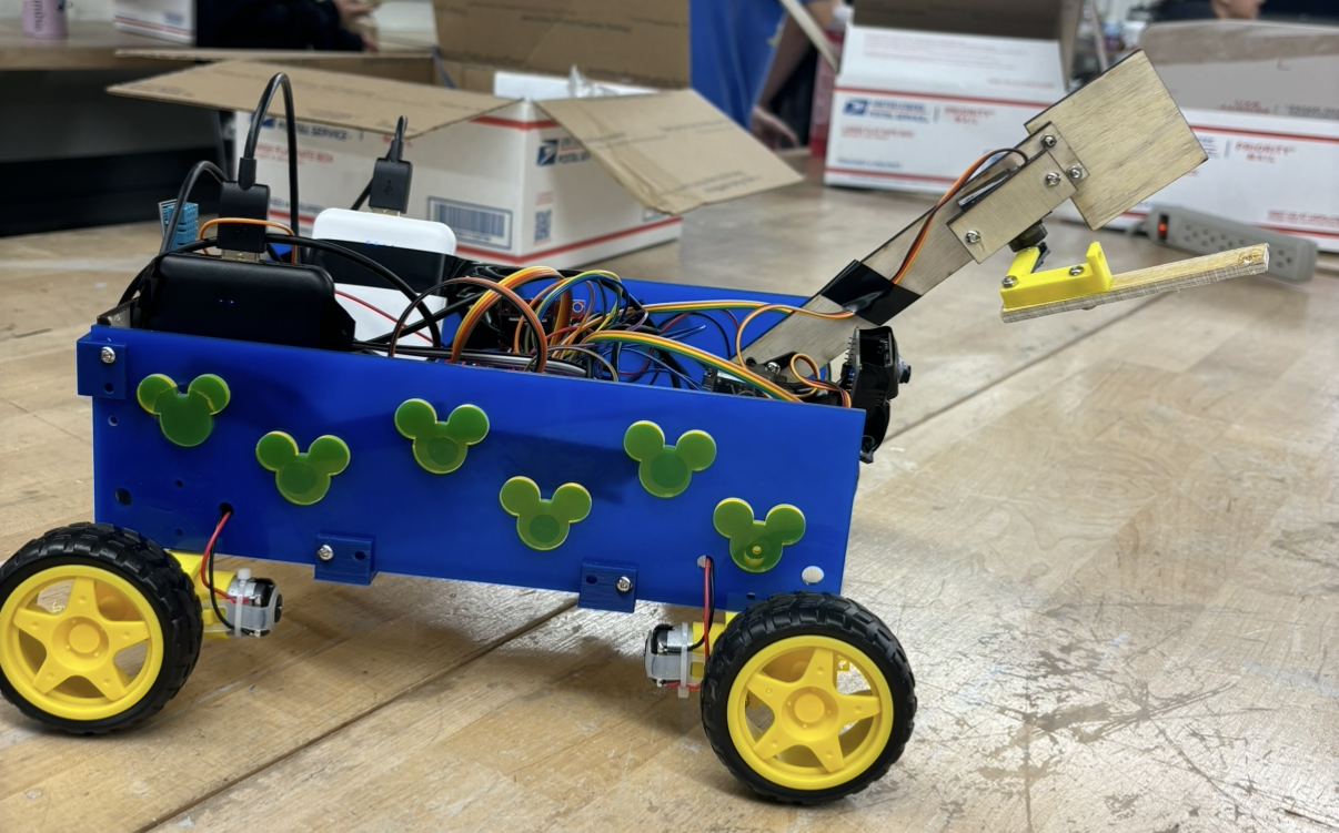 Completed rover on a workbench showing blue chassis, yellow wheels, exposed electronics, and raised wooden arm