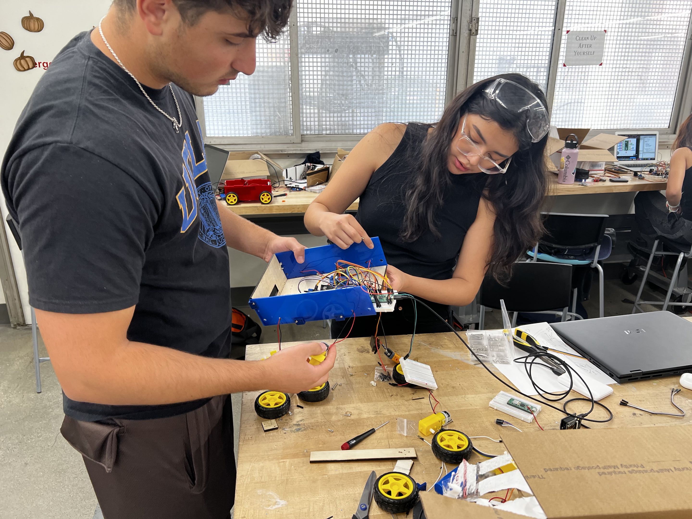 Student team members holding the rover chassis while working on motors and wiring at a workbench