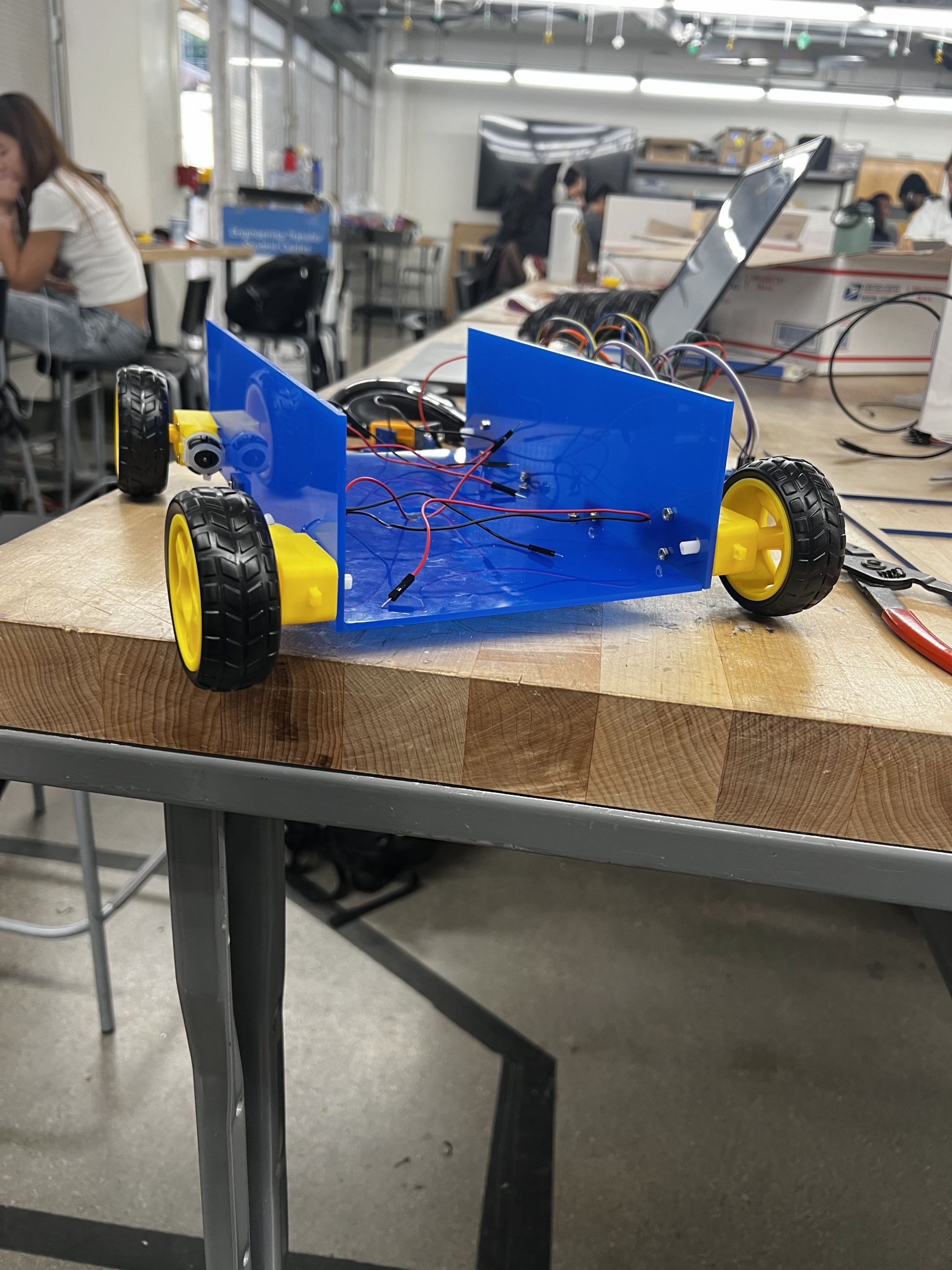 First rover iteration: open blue chassis with four wheels, motors, and loose wiring on a workbench